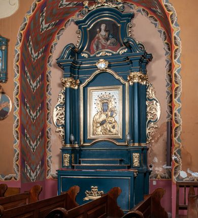 Zdjęcie nr 3: Ołtarz przyścienny, architektoniczny, jednokondygnacyjny, jednoosiowy, ze zwieńczeniem. Mensa w formie prostopadłościanu. Antepedium drewniane, w centrum złocony ormament roślinny oraz banderola.  Retabulum ustawione na zdwojonym cokole, flankowane kolumnami, ustawionych na tle zwielokrotnionych pilastrów podtrzymujących wyłamane belkowanie, na osi kolumn przerwany wolutowy przyczółek. W polu głównym nastawy płytka wnęka, ujęta złoconą i profilowaną ramą w kształcie stojącego prostokąta zamkniętego łukiem wklęsło-wypukłym z uskokami. Pośrodku obraz Matki Boskiej Częstochowskiej. W górnej części ramy złocony kartusz. Zwieńczenie o delikatnie wklęsłych bokach ze spływami wolutowymi, zamknięte łukiem nadwieszonym. Nad nim złocona muszla palmetowa ujęta dwoma spływami wolutowymi. W polu zwieńczenia obraz św. Barbary w ramie o fantazyjnym wykroju. Retabulum flankowane po bokach ażurowymi uszami utworzonymi z liści akantu. Podpory ustawione na bazach, kapitele kompozytowe, trzony kolumn gładkie, natomiast trzony pilastrów kanelowane. Struktura malowana w kolorze ciemnozielonym, ornamenty i detale złocone.