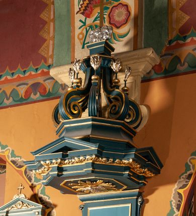 Zdjęcie nr 4: Ambona zawieszona na południowej ścianie pomiędzy ołtarzem św. Franciszka z Asyżu, a ołtarzem św. Kingi, dostępna schodami z grubości muru. Kosz na planie ośmioboku, z wypukłą dolną częścią podstawy zdobionej owalnymi, pustymi medalionami ujętymi uproszczonym puklowaniem. Ścianki kosza zdobione prostokątnymi płycinami, flankowanymi pilastrami o trzonach wypełnionych rzędem kampanul. Parapet kosza w formie prostego, profilowanego gzymsu. Zaplecek w kształcie stojącego prostokąta, dwudzielny, w każdej części dekorowany prostokątną płyciną, ujęty po bokach spływami wolutowymi. Baldachim na planie ośmioboku, z trzech stron z trójkątnymi przyczółkami, zaś belkowanie zdobione wicią liści akantu. W podniebiu baldachimu, w ośmiobocznej płycinie umieszczona gołębica Ducha Świętego na tle promienistej glorii. Zwieńczenie w kształcie sześciu wolut spiętych w kabłąk, przechodzących w prostopadłościenny szczyt z krzyżem łacińskim zatkniętym na obłokach. Każda z wolut zdobiona małym wazonikiem z listkami akantu. Struktura polichromowana na kolor ciemnozielony, detale i ornamentyka złocone i srebrzone. 

