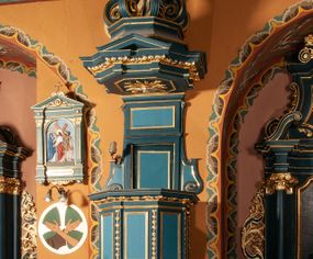 Zdjęcie nr 1: Ambona zawieszona na południowej ścianie pomiędzy ołtarzem św. Franciszka z Asyżu, a ołtarzem św. Kingi, dostępna schodami z grubości muru. Kosz na planie ośmioboku, z wypukłą dolną częścią podstawy zdobionej owalnymi, pustymi medalionami ujętymi uproszczonym puklowaniem. Ścianki kosza zdobione prostokątnymi płycinami, flankowanymi pilastrami o trzonach wypełnionych rzędem kampanul. Parapet kosza w formie prostego, profilowanego gzymsu. Zaplecek w kształcie stojącego prostokąta, dwudzielny, w każdej części dekorowany prostokątną płyciną, ujęty po bokach spływami wolutowymi. Baldachim na planie ośmioboku, z trzech stron z trójkątnymi przyczółkami, zaś belkowanie zdobione wicią liści akantu. W podniebiu baldachimu, w ośmiobocznej płycinie umieszczona gołębica Ducha Świętego na tle promienistej glorii. Zwieńczenie w kształcie sześciu wolut spiętych w kabłąk, przechodzących w prostopadłościenny szczyt z krzyżem łacińskim zatkniętym na obłokach. Każda z wolut zdobiona małym wazonikiem z listkami akantu. Struktura polichromowana na kolor ciemnozielony, detale i ornamentyka złocone i srebrzone. 

