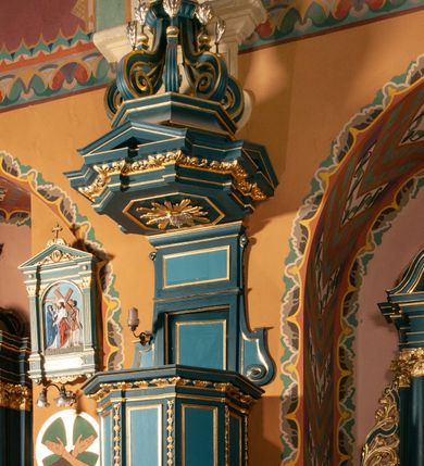 Zdjęcie nr 3: Ambona zawieszona na południowej ścianie pomiędzy ołtarzem św. Franciszka z Asyżu, a ołtarzem św. Kingi, dostępna schodami z grubości muru. Kosz na planie ośmioboku, z wypukłą dolną częścią podstawy zdobionej owalnymi, pustymi medalionami ujętymi uproszczonym puklowaniem. Ścianki kosza zdobione prostokątnymi płycinami, flankowanymi pilastrami o trzonach wypełnionych rzędem kampanul. Parapet kosza w formie prostego, profilowanego gzymsu. Zaplecek w kształcie stojącego prostokąta, dwudzielny, w każdej części dekorowany prostokątną płyciną, ujęty po bokach spływami wolutowymi. Baldachim na planie ośmioboku, z trzech stron z trójkątnymi przyczółkami, zaś belkowanie zdobione wicią liści akantu. W podniebiu baldachimu, w ośmiobocznej płycinie umieszczona gołębica Ducha Świętego na tle promienistej glorii. Zwieńczenie w kształcie sześciu wolut spiętych w kabłąk, przechodzących w prostopadłościenny szczyt z krzyżem łacińskim zatkniętym na obłokach. Każda z wolut zdobiona małym wazonikiem z listkami akantu. Struktura polichromowana na kolor ciemnozielony, detale i ornamentyka złocone i srebrzone. 

