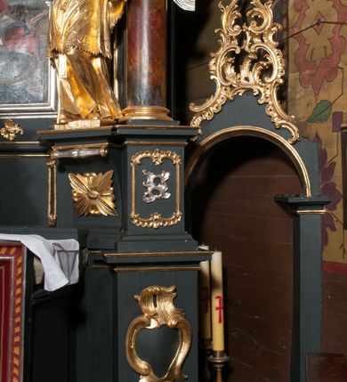 Zdjęcie nr 18: Nastawa architektoniczna, jednoosiowa z bramkami, jednokondygnacyjna ze zwieńczeniem, na dwustrefowym cokole. Ołtarz drewniany prostopadłościenny z kamienną mensą. Antepedium ujęte profilowaną ramą, wykonane z czerwonego, haftowanego aksamitu, w centrum medalion z przedstawieniem baranka leżącego na księdze, w dolnych narożach motywy kwiatowe. 
Retabulum flankowane ustawionymi pod kątem na zewnątrz dwiema parami korynckich kolumn, umieszczonych na tle kanelowanych pilastrów. Kolumny ustawione na cokołach, podtrzymują wyłamane belkowanie, przerwane nad polem środkowym, oraz przerwany falisty przyczółek. Na belkowaniu stoi para wazonów, na przerwanym przyczółku siedzą dwa putta. Pomiędzy kolumnami na cokołach znajdują się figury św. Jana Kantego i św. Jana Nepomucena. W polu głównym obraz z przedstawieniem św. Sebastiana ujęty profilowaną ramą w formie stojącego prostokąta zamkniętego łukiem półkolistym nadwieszonym z uskokiem, zwieńczoną rokokowym kartuszem flankowanym kwiatowymi zwisami. Zwieńczenie w formie stojącego prostokąta ujęte pilastrami o trzonach przechodzących w spływy wolutowe, zamknięte rokokowym kartuszem. W polu przedstawienie św. Floriana w profilowanej ramie w formie stojącego prostokąta zamkniętego łukiem półkolistym nadwieszonym. Bramki na wysokości cokołu nastawy w formie arkad podtrzymywanych przez pilastry, zwieńczonych racaille&#039;owymi szczytami. Dwustrefowy cokół dekorowany rokokowymi płycinami, rocaille&#039;m, rozetami i kartuszami. Kanelowane pilastry nastawy ozdobione kampanulami oraz bogatymi, kwiatowymi zwisami. Nastawa ujęta małymi uszami utworzonymi z liści palmy. 
Struktura architektoniczna polichromowana w kolorze czarnym, trzony kolumn pokryte polichromią imitującą kolorową marmoryzację, dekoracja rzeźbiarska, ornamentalna oraz profile pozłacane i posrebrzane. 

