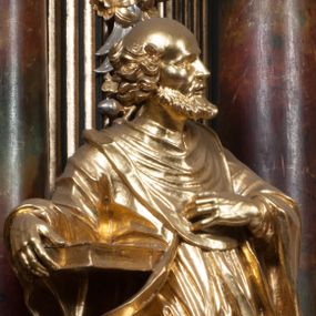 Zdjęcie nr 1: Rzeźba jest ścięta i wydrążona z tyłu, ustawiona na nieregularnej podstawie. Figura zwrócona jest frontalnie, w kontrapoście, z lekko pochylonymi głową i torsem, skierowanymi w lewo. Święty prawą ręką trzyma księgę opartą o jego biodro, lewą dłoń kładzie na piersi. Twarz ma wychudzoną, z podkreślonymi kośćmi policzkowymi, migdałowatymi, głęboko osadzonymi oczami, wąskim, małym nosem o ostrym profilu oraz wąskimi, otwartymi ustami, okoloną krótką, gęstą brodą, silnie wysuniętą do przodu oraz kręconymi włosami po bokach i z tyłu głowy. Święty ubrany jest w długą silnie fałdowaną tunikę oraz togę rektorską o szerokich rękawach, rozchyloną z przodu postaci z zygzakowato układającą się fałdą na jego prawej nodze. Figura w całości pozłocona. 
