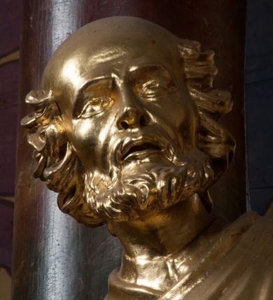 Zdjęcie nr 7: Rzeźba jest ścięta i wydrążona z tyłu, ustawiona na nieregularnej podstawie. Figura zwrócona jest frontalnie, w kontrapoście, z lekko pochylonymi głową i torsem, skierowanymi w lewo. Święty prawą ręką trzyma księgę opartą o jego biodro, lewą dłoń kładzie na piersi. Twarz ma wychudzoną, z podkreślonymi kośćmi policzkowymi, migdałowatymi, głęboko osadzonymi oczami, wąskim, małym nosem o ostrym profilu oraz wąskimi, otwartymi ustami, okoloną krótką, gęstą brodą, silnie wysuniętą do przodu oraz kręconymi włosami po bokach i z tyłu głowy. Święty ubrany jest w długą silnie fałdowaną tunikę oraz togę rektorską o szerokich rękawach, rozchyloną z przodu postaci z zygzakowato układającą się fałdą na jego prawej nodze. Figura w całości pozłocona. 
