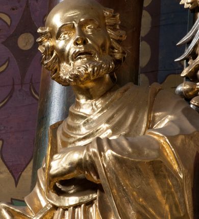 Zdjęcie nr 6: Rzeźba jest ścięta i wydrążona z tyłu, ustawiona na nieregularnej podstawie. Figura zwrócona jest frontalnie, w kontrapoście, z lekko pochylonymi głową i torsem, skierowanymi w lewo. Święty prawą ręką trzyma księgę opartą o jego biodro, lewą dłoń kładzie na piersi. Twarz ma wychudzoną, z podkreślonymi kośćmi policzkowymi, migdałowatymi, głęboko osadzonymi oczami, wąskim, małym nosem o ostrym profilu oraz wąskimi, otwartymi ustami, okoloną krótką, gęstą brodą, silnie wysuniętą do przodu oraz kręconymi włosami po bokach i z tyłu głowy. Święty ubrany jest w długą silnie fałdowaną tunikę oraz togę rektorską o szerokich rękawach, rozchyloną z przodu postaci z zygzakowato układającą się fałdą na jego prawej nodze. Figura w całości pozłocona. 
