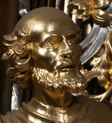 Zdjęcie nr 9: Rzeźba jest ścięta i wydrążona z tyłu, ustawiona na nieregularnej podstawie. Figura zwrócona jest frontalnie, w kontrapoście, z lekko pochylonymi głową i torsem, skierowanymi w lewo. Święty prawą ręką trzyma księgę opartą o jego biodro, lewą dłoń kładzie na piersi. Twarz ma wychudzoną, z podkreślonymi kośćmi policzkowymi, migdałowatymi, głęboko osadzonymi oczami, wąskim, małym nosem o ostrym profilu oraz wąskimi, otwartymi ustami, okoloną krótką, gęstą brodą, silnie wysuniętą do przodu oraz kręconymi włosami po bokach i z tyłu głowy. Święty ubrany jest w długą silnie fałdowaną tunikę oraz togę rektorską o szerokich rękawach, rozchyloną z przodu postaci z zygzakowato układającą się fałdą na jego prawej nodze. Figura w całości pozłocona. 
