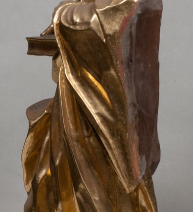 Zdjęcie nr 10: Rzeźba jest ścięta i wydrążona z tyłu, ustawiona na nieregularnej podstawie. Figura zwrócona jest frontalnie, w kontrapoście, z lekko pochylonymi głową i torsem, skierowanymi w lewo. Święty prawą ręką trzyma księgę opartą o jego biodro, lewą dłoń kładzie na piersi. Twarz ma wychudzoną, z podkreślonymi kośćmi policzkowymi, migdałowatymi, głęboko osadzonymi oczami, wąskim, małym nosem o ostrym profilu oraz wąskimi, otwartymi ustami, okoloną krótką, gęstą brodą, silnie wysuniętą do przodu oraz kręconymi włosami po bokach i z tyłu głowy. Święty ubrany jest w długą silnie fałdowaną tunikę oraz togę rektorską o szerokich rękawach, rozchyloną z przodu postaci z zygzakowato układającą się fałdą na jego prawej nodze. Figura w całości pozłocona. 
