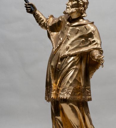 Zdjęcie nr 13: Rzeźba jest ścięta z tyłu i drążona, ustawiona na nieregularnej podstawie. Figura zwrócona jest frontalnie, w kontrapoście, z odchylonym w tył torsem i uniesioną głową, skierowaną w prawo. W prawej uniesionej wysoko ręce trzyma krucyfiks, lewą opuszczoną, wyciąga w bok. Twarz świętego jest szczupła, z uwypuklonymi kośćmi policzkowymi, migdałowatymi, głęboko osadzonymi oczami, wąskim, małym nosie o ostrym profilu oraz rozchylonymi, wąskimi ustami; okolona jest krótką, gęstą brodą wysuniętą do przodu oraz kręconymi, krótkimi włosami. Jan Nepomucen jest ubrany w długą sutannę, komżę dekorowaną przy dolnej krawędzi płaskorzeźbionym rocaille&#039;m oraz w zawiązaną na piersi almucję. Figura jest w całości pozłocona. 






