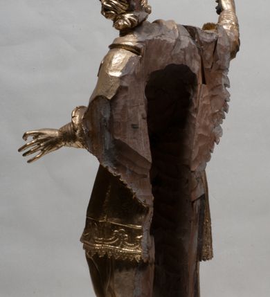 Zdjęcie nr 9: Rzeźba jest ścięta z tyłu i drążona, ustawiona na nieregularnej podstawie. Figura zwrócona jest frontalnie, w kontrapoście, z odchylonym w tył torsem i uniesioną głową, skierowaną w prawo. W prawej uniesionej wysoko ręce trzyma krucyfiks, lewą opuszczoną, wyciąga w bok. Twarz świętego jest szczupła, z uwypuklonymi kośćmi policzkowymi, migdałowatymi, głęboko osadzonymi oczami, wąskim, małym nosie o ostrym profilu oraz rozchylonymi, wąskimi ustami; okolona jest krótką, gęstą brodą wysuniętą do przodu oraz kręconymi, krótkimi włosami. Jan Nepomucen jest ubrany w długą sutannę, komżę dekorowaną przy dolnej krawędzi płaskorzeźbionym rocaille&#039;m oraz w zawiązaną na piersi almucję. Figura jest w całości pozłocona. 






