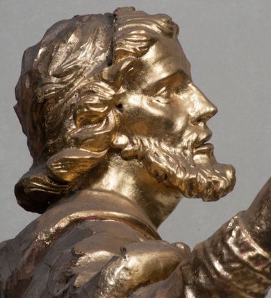 Zdjęcie nr 15: Rzeźba jest ścięta z tyłu i drążona, ustawiona na nieregularnej podstawie. Figura zwrócona jest frontalnie, w kontrapoście, z odchylonym w tył torsem i uniesioną głową, skierowaną w prawo. W prawej uniesionej wysoko ręce trzyma krucyfiks, lewą opuszczoną, wyciąga w bok. Twarz świętego jest szczupła, z uwypuklonymi kośćmi policzkowymi, migdałowatymi, głęboko osadzonymi oczami, wąskim, małym nosie o ostrym profilu oraz rozchylonymi, wąskimi ustami; okolona jest krótką, gęstą brodą wysuniętą do przodu oraz kręconymi, krótkimi włosami. Jan Nepomucen jest ubrany w długą sutannę, komżę dekorowaną przy dolnej krawędzi płaskorzeźbionym rocaille&#039;m oraz w zawiązaną na piersi almucję. Figura jest w całości pozłocona. 






