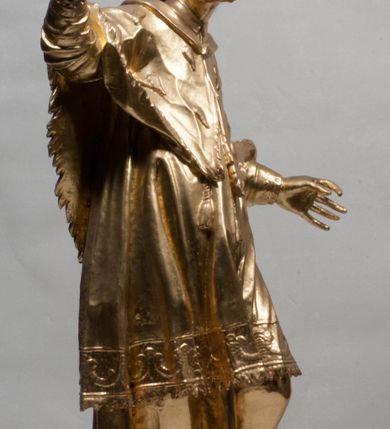 Zdjęcie nr 10: Rzeźba jest ścięta z tyłu i drążona, ustawiona na nieregularnej podstawie. Figura zwrócona jest frontalnie, w kontrapoście, z odchylonym w tył torsem i uniesioną głową, skierowaną w prawo. W prawej uniesionej wysoko ręce trzyma krucyfiks, lewą opuszczoną, wyciąga w bok. Twarz świętego jest szczupła, z uwypuklonymi kośćmi policzkowymi, migdałowatymi, głęboko osadzonymi oczami, wąskim, małym nosie o ostrym profilu oraz rozchylonymi, wąskimi ustami; okolona jest krótką, gęstą brodą wysuniętą do przodu oraz kręconymi, krótkimi włosami. Jan Nepomucen jest ubrany w długą sutannę, komżę dekorowaną przy dolnej krawędzi płaskorzeźbionym rocaille'm oraz w zawiązaną na piersi almucję. Figura jest w całości pozłocona. 






