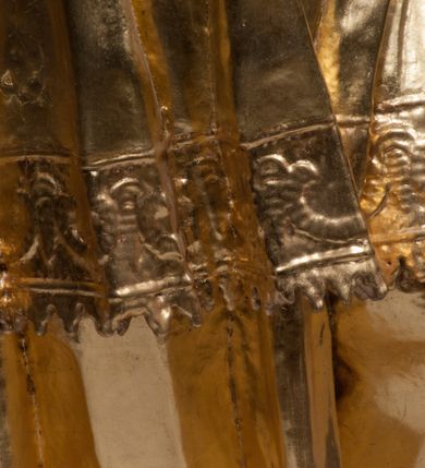 Zdjęcie nr 18: Rzeźba jest ścięta z tyłu i drążona, ustawiona na nieregularnej podstawie. Figura zwrócona jest frontalnie, w kontrapoście, z odchylonym w tył torsem i uniesioną głową, skierowaną w prawo. W prawej uniesionej wysoko ręce trzyma krucyfiks, lewą opuszczoną, wyciąga w bok. Twarz świętego jest szczupła, z uwypuklonymi kośćmi policzkowymi, migdałowatymi, głęboko osadzonymi oczami, wąskim, małym nosie o ostrym profilu oraz rozchylonymi, wąskimi ustami; okolona jest krótką, gęstą brodą wysuniętą do przodu oraz kręconymi, krótkimi włosami. Jan Nepomucen jest ubrany w długą sutannę, komżę dekorowaną przy dolnej krawędzi płaskorzeźbionym rocaille&#039;m oraz w zawiązaną na piersi almucję. Figura jest w całości pozłocona. 






