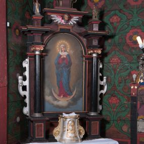 Zdjęcie nr 1: Nastawa ołtarzowa architektoniczna, jednokondygnacyjna, jednoosiowa na cokole. Ołtarz drewniany, prostopadłościenny, mensa drewniana. Antepedium w formie haftowanej maszynowo tkaniny. Nastawa ujęta parą pilastrów i parą stojących przed nimi kolumn o jońskich kapitelach dźwigających imposty o silnie wysuniętym gzymsie, na którym stoją dwa cokoły z figurami św. Biskupa i św. Floriana. Pole główne w całości wypełnione półkolistą arkadą podtrzymywaną na węgarach, zakończoną fragmentem gzymsu z uskrzydloną główką anielską. W polu obraz w formie stojącego prostokąta zamkniętego półkoliście z przedstawieniem Najświętszej Marii Panny Niepokalanie Poczętej. Kondygnacja zakończona fragmentem gzymsu, na którym stoi ośmioboczny cokół ujęty w narożach wolutami z koroną zamkniętą, zakończoną krzyżem. Nastawa ujęta uszami utworzonymi z ornamentu okuciowego. Struktura architektoniczna polichromowana na czarno, płyciny w kolorze czerwono-brązowym, profile pozłocone, uszy posrebrzone. 

