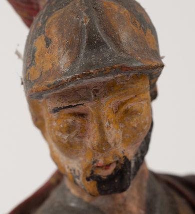 Zdjęcie nr 11: Figurka pełnoplastyczna, ustawiona na niewysokim, profilowanym cokole na planie prostokąta. Święty przedstawiony w całej postaci, zwrócony jest frontalnie, w wykroku, lekko pochylony w prawą stronę. Lewą ręką przytrzymuje przy boku chorągiew, prawą trzyma cebrzyk, z którego wylewa wodę na palący się budynek. Twarz ma szczupłą, okoloną krótką brodą. Ubrany jest w strój żołnierza: tunikę sięgającą kolan, zbroję torsową, na plecy ma zarzucony płaszcz, na głowie ma hełm z pióropuszem. Przy jego prawej nodze znajduje się niewielki budynek w płomieniach. Polichromia ciała naturalistyczna, broda brązowa, elementy stroju i chorągiew szaro-niebieskie z żółtymi detalami, płaszcz i pióropusz czerwone. 


