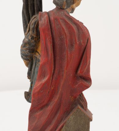 Zdjęcie nr 8: Figurka pełnoplastyczna, ustawiona na niewysokim, profilowanym cokole na planie prostokąta. Święty przedstawiony w całej postaci, zwrócony jest frontalnie, w wykroku, lekko pochylony w prawą stronę. Lewą ręką przytrzymuje przy boku chorągiew, prawą trzyma cebrzyk, z którego wylewa wodę na palący się budynek. Twarz ma szczupłą, okoloną krótką brodą. Ubrany jest w strój żołnierza: tunikę sięgającą kolan, zbroję torsową, na plecy ma zarzucony płaszcz, na głowie ma hełm z pióropuszem. Przy jego prawej nodze znajduje się niewielki budynek w płomieniach. Polichromia ciała naturalistyczna, broda brązowa, elementy stroju i chorągiew szaro-niebieskie z żółtymi detalami, płaszcz i pióropusz czerwone. 


