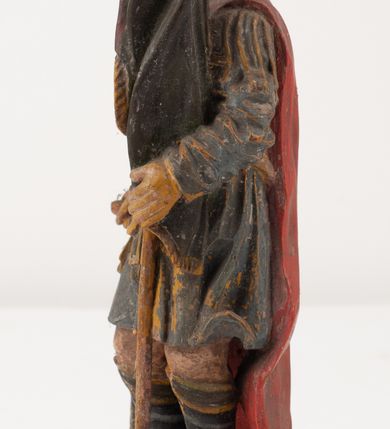 Zdjęcie nr 3: Figurka pełnoplastyczna, ustawiona na niewysokim, profilowanym cokole na planie prostokąta. Święty przedstawiony w całej postaci, zwrócony jest frontalnie, w wykroku, lekko pochylony w prawą stronę. Lewą ręką przytrzymuje przy boku chorągiew, prawą trzyma cebrzyk, z którego wylewa wodę na palący się budynek. Twarz ma szczupłą, okoloną krótką brodą. Ubrany jest w strój żołnierza: tunikę sięgającą kolan, zbroję torsową, na plecy ma zarzucony płaszcz, na głowie ma hełm z pióropuszem. Przy jego prawej nodze znajduje się niewielki budynek w płomieniach. Polichromia ciała naturalistyczna, broda brązowa, elementy stroju i chorągiew szaro-niebieskie z żółtymi detalami, płaszcz i pióropusz czerwone. 


