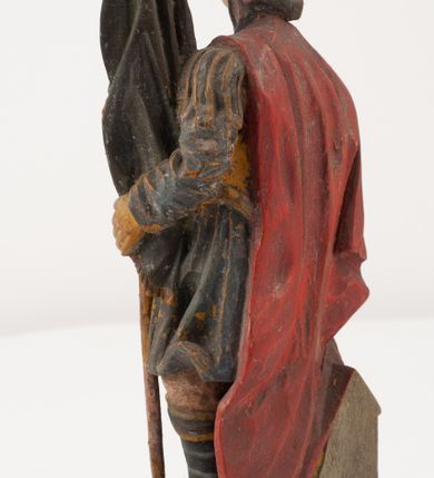 Zdjęcie nr 7: Figurka pełnoplastyczna, ustawiona na niewysokim, profilowanym cokole na planie prostokąta. Święty przedstawiony w całej postaci, zwrócony jest frontalnie, w wykroku, lekko pochylony w prawą stronę. Lewą ręką przytrzymuje przy boku chorągiew, prawą trzyma cebrzyk, z którego wylewa wodę na palący się budynek. Twarz ma szczupłą, okoloną krótką brodą. Ubrany jest w strój żołnierza: tunikę sięgającą kolan, zbroję torsową, na plecy ma zarzucony płaszcz, na głowie ma hełm z pióropuszem. Przy jego prawej nodze znajduje się niewielki budynek w płomieniach. Polichromia ciała naturalistyczna, broda brązowa, elementy stroju i chorągiew szaro-niebieskie z żółtymi detalami, płaszcz i pióropusz czerwone. 


