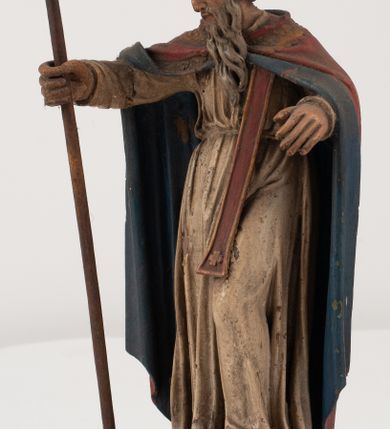 Zdjęcie nr 2: Figura jest pełnoplastyczna, ustawiona na profilowanym cokole na planie prostokąta. Święty przedstawiony w całej postaci, zwrócony jest frontalnie, w kontrapoście, z głową skierowaną w prawo. Obie ręce wyciąga przed siebie, w prawej trzyma pastorał. Twarz ma pociągłą, o  oczach skierowanych w dół, dużym, garbatym nosie i niewielkich ustach, okoloną długą brodą uformowaną w pojedyncze pukle, opadającą na pierś oraz krótkimi, silnie kręconymi włosami. Święty ubrany jest w strój biskupa: białą albę przepasaną w talii, czerwoną stułę, czerwoną kapę z niebieską podszewką, zapiętą na piersi, na głowie ma czerwoną infułę. Polichromia ciała naturalistyczna. 
