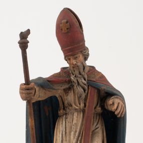 Zdjęcie nr 1: Figura jest pełnoplastyczna, ustawiona na profilowanym cokole na planie prostokąta. Święty przedstawiony w całej postaci, zwrócony jest frontalnie, w kontrapoście, z głową skierowaną w prawo. Obie ręce wyciąga przed siebie, w prawej trzyma pastorał. Twarz ma pociągłą, o  oczach skierowanych w dół, dużym, garbatym nosie i niewielkich ustach, okoloną długą brodą uformowaną w pojedyncze pukle, opadającą na pierś oraz krótkimi, silnie kręconymi włosami. Święty ubrany jest w strój biskupa: białą albę przepasaną w talii, czerwoną stułę, czerwoną kapę z niebieską podszewką, zapiętą na piersi, na głowie ma czerwoną infułę. Polichromia ciała naturalistyczna. 
