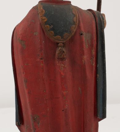 Zdjęcie nr 10: Figura jest pełnoplastyczna, ustawiona na profilowanym cokole na planie prostokąta. Święty przedstawiony w całej postaci, zwrócony jest frontalnie, w kontrapoście, z głową skierowaną w prawo. Obie ręce wyciąga przed siebie, w prawej trzyma pastorał. Twarz ma pociągłą, o  oczach skierowanych w dół, dużym, garbatym nosie i niewielkich ustach, okoloną długą brodą uformowaną w pojedyncze pukle, opadającą na pierś oraz krótkimi, silnie kręconymi włosami. Święty ubrany jest w strój biskupa: białą albę przepasaną w talii, czerwoną stułę, czerwoną kapę z niebieską podszewką, zapiętą na piersi, na głowie ma czerwoną infułę. Polichromia ciała naturalistyczna. 
