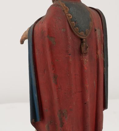 Zdjęcie nr 9: Figura jest pełnoplastyczna, ustawiona na profilowanym cokole na planie prostokąta. Święty przedstawiony w całej postaci, zwrócony jest frontalnie, w kontrapoście, z głową skierowaną w prawo. Obie ręce wyciąga przed siebie, w prawej trzyma pastorał. Twarz ma pociągłą, o  oczach skierowanych w dół, dużym, garbatym nosie i niewielkich ustach, okoloną długą brodą uformowaną w pojedyncze pukle, opadającą na pierś oraz krótkimi, silnie kręconymi włosami. Święty ubrany jest w strój biskupa: białą albę przepasaną w talii, czerwoną stułę, czerwoną kapę z niebieską podszewką, zapiętą na piersi, na głowie ma czerwoną infułę. Polichromia ciała naturalistyczna. 
