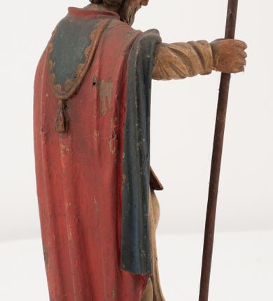 Zdjęcie nr 8: Figura jest pełnoplastyczna, ustawiona na profilowanym cokole na planie prostokąta. Święty przedstawiony w całej postaci, zwrócony jest frontalnie, w kontrapoście, z głową skierowaną w prawo. Obie ręce wyciąga przed siebie, w prawej trzyma pastorał. Twarz ma pociągłą, o  oczach skierowanych w dół, dużym, garbatym nosie i niewielkich ustach, okoloną długą brodą uformowaną w pojedyncze pukle, opadającą na pierś oraz krótkimi, silnie kręconymi włosami. Święty ubrany jest w strój biskupa: białą albę przepasaną w talii, czerwoną stułę, czerwoną kapę z niebieską podszewką, zapiętą na piersi, na głowie ma czerwoną infułę. Polichromia ciała naturalistyczna. 
