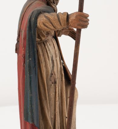 Zdjęcie nr 6: Figura jest pełnoplastyczna, ustawiona na profilowanym cokole na planie prostokąta. Święty przedstawiony w całej postaci, zwrócony jest frontalnie, w kontrapoście, z głową skierowaną w prawo. Obie ręce wyciąga przed siebie, w prawej trzyma pastorał. Twarz ma pociągłą, o  oczach skierowanych w dół, dużym, garbatym nosie i niewielkich ustach, okoloną długą brodą uformowaną w pojedyncze pukle, opadającą na pierś oraz krótkimi, silnie kręconymi włosami. Święty ubrany jest w strój biskupa: białą albę przepasaną w talii, czerwoną stułę, czerwoną kapę z niebieską podszewką, zapiętą na piersi, na głowie ma czerwoną infułę. Polichromia ciała naturalistyczna. 
