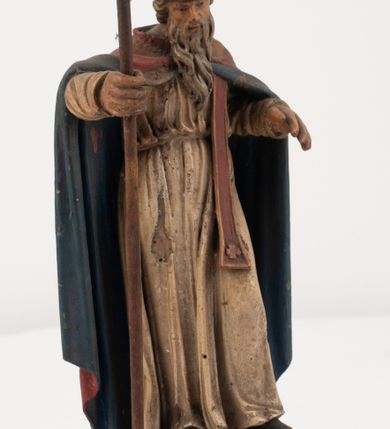 Zdjęcie nr 4: Figura jest pełnoplastyczna, ustawiona na profilowanym cokole na planie prostokąta. Święty przedstawiony w całej postaci, zwrócony jest frontalnie, w kontrapoście, z głową skierowaną w prawo. Obie ręce wyciąga przed siebie, w prawej trzyma pastorał. Twarz ma pociągłą, o  oczach skierowanych w dół, dużym, garbatym nosie i niewielkich ustach, okoloną długą brodą uformowaną w pojedyncze pukle, opadającą na pierś oraz krótkimi, silnie kręconymi włosami. Święty ubrany jest w strój biskupa: białą albę przepasaną w talii, czerwoną stułę, czerwoną kapę z niebieską podszewką, zapiętą na piersi, na głowie ma czerwoną infułę. Polichromia ciała naturalistyczna. 
