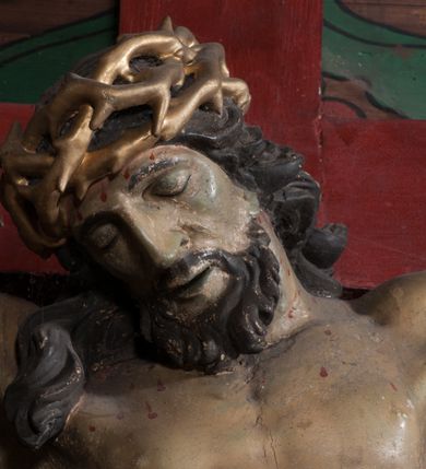 Zdjęcie nr 4: Figura umarłego Chrystusa przybita jest trzema gwoździami do prostego krzyża. Ciało w lekkim zwisie, o szeroko rozłożonych ramionach, układających się w delikatny łuk, głowa opada bezwładnie na prawe ramię, nogi są delikatnie ugięte w kolanach, stopy skrzyżowane w układzie prawa na lewą. Twarz pociągła, o łagodnych rysach i niskim czole, zamkniętych oczach, dużym nosie i rozchylonych ustach, okolona krótką, rozdwajającą się brodą oraz silnie kręconymi włosami opadającymi na prawy bark. Na głowie korona cierniowa. Ciało wychudzone, smukłe, o miękko modelowanej muskulaturze oraz silnie zaznaczonych żebrach i mostku klatki piersiowej, z podkreślonymi liniami ścięgien w partiach ramion i nóg. Biodra przepasane ekspresyjnie drapowanym perizonium zawieszonym na podwójnym sznurze, sięgającym połowy ud, odsłaniającym prawe biodro, ze zwisem rozwianej tkaniny na prawym boku. Polichromia naturalistyczna w partiach ciała z zaznaczonymi śladami męki, perizonium i korona cierniowa pozłacane. W górnej części krzyża banderola z inskrypcją „I.N. / R.I.”.



