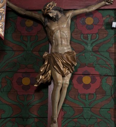 Zdjęcie nr 3: Figura umarłego Chrystusa przybita jest trzema gwoździami do prostego krzyża. Ciało w lekkim zwisie, o szeroko rozłożonych ramionach, układających się w delikatny łuk, głowa opada bezwładnie na prawe ramię, nogi są delikatnie ugięte w kolanach, stopy skrzyżowane w układzie prawa na lewą. Twarz pociągła, o łagodnych rysach i niskim czole, zamkniętych oczach, dużym nosie i rozchylonych ustach, okolona krótką, rozdwajającą się brodą oraz silnie kręconymi włosami opadającymi na prawy bark. Na głowie korona cierniowa. Ciało wychudzone, smukłe, o miękko modelowanej muskulaturze oraz silnie zaznaczonych żebrach i mostku klatki piersiowej, z podkreślonymi liniami ścięgien w partiach ramion i nóg. Biodra przepasane ekspresyjnie drapowanym perizonium zawieszonym na podwójnym sznurze, sięgającym połowy ud, odsłaniającym prawe biodro, ze zwisem rozwianej tkaniny na prawym boku. Polichromia naturalistyczna w partiach ciała z zaznaczonymi śladami męki, perizonium i korona cierniowa pozłacane. W górnej części krzyża banderola z inskrypcją „I.N. / R.I.”.



