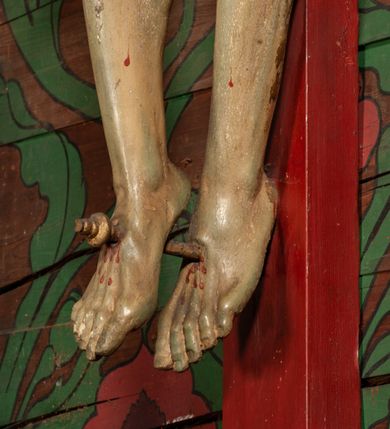 Zdjęcie nr 7: Figura umarłego Chrystusa przybita jest trzema gwoździami do prostego krzyża. Ciało w lekkim zwisie, o szeroko rozłożonych ramionach, układających się w delikatny łuk, głowa opada bezwładnie na prawe ramię, nogi są delikatnie ugięte w kolanach, stopy skrzyżowane w układzie prawa na lewą. Twarz pociągła, o łagodnych rysach i niskim czole, zamkniętych oczach, dużym nosie i rozchylonych ustach, okolona krótką, rozdwajającą się brodą oraz silnie kręconymi włosami opadającymi na prawy bark. Na głowie korona cierniowa. Ciało wychudzone, smukłe, o miękko modelowanej muskulaturze oraz silnie zaznaczonych żebrach i mostku klatki piersiowej, z podkreślonymi liniami ścięgien w partiach ramion i nóg. Biodra przepasane ekspresyjnie drapowanym perizonium zawieszonym na podwójnym sznurze, sięgającym połowy ud, odsłaniającym prawe biodro, ze zwisem rozwianej tkaniny na prawym boku. Polichromia naturalistyczna w partiach ciała z zaznaczonymi śladami męki, perizonium i korona cierniowa pozłacane. W górnej części krzyża banderola z inskrypcją „I.N. / R.I.”.




