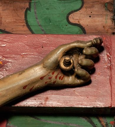 Zdjęcie nr 10: Figura umarłego Chrystusa przybita jest trzema gwoździami do prostego krzyża. Ciało w lekkim zwisie, o szeroko rozłożonych ramionach, układających się w delikatny łuk, głowa opada bezwładnie na prawe ramię, nogi są delikatnie ugięte w kolanach, stopy skrzyżowane w układzie prawa na lewą. Twarz pociągła, o łagodnych rysach i niskim czole, zamkniętych oczach, dużym nosie i rozchylonych ustach, okolona krótką, rozdwajającą się brodą oraz silnie kręconymi włosami opadającymi na prawy bark. Na głowie korona cierniowa. Ciało wychudzone, smukłe, o miękko modelowanej muskulaturze oraz silnie zaznaczonych żebrach i mostku klatki piersiowej, z podkreślonymi liniami ścięgien w partiach ramion i nóg. Biodra przepasane ekspresyjnie drapowanym perizonium zawieszonym na podwójnym sznurze, sięgającym połowy ud, odsłaniającym prawe biodro, ze zwisem rozwianej tkaniny na prawym boku. Polichromia naturalistyczna w partiach ciała z zaznaczonymi śladami męki, perizonium i korona cierniowa pozłacane. W górnej części krzyża banderola z inskrypcją „I.N. / R.I.”.



