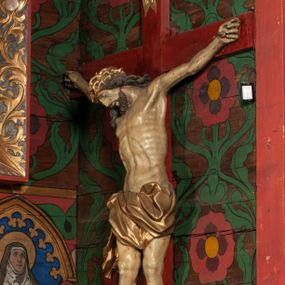 Zdjęcie nr 1: Figura umarłego Chrystusa przybita jest trzema gwoździami do prostego krzyża. Ciało w lekkim zwisie, o szeroko rozłożonych ramionach, układających się w delikatny łuk, głowa opada bezwładnie na prawe ramię, nogi są delikatnie ugięte w kolanach, stopy skrzyżowane w układzie prawa na lewą. Twarz pociągła, o łagodnych rysach i niskim czole, zamkniętych oczach, dużym nosie i rozchylonych ustach, okolona krótką, rozdwajającą się brodą oraz silnie kręconymi włosami opadającymi na prawy bark. Na głowie korona cierniowa. Ciało wychudzone, smukłe, o miękko modelowanej muskulaturze oraz silnie zaznaczonych żebrach i mostku klatki piersiowej, z podkreślonymi liniami ścięgien w partiach ramion i nóg. Biodra przepasane ekspresyjnie drapowanym perizonium zawieszonym na podwójnym sznurze, sięgającym połowy ud, odsłaniającym prawe biodro, ze zwisem rozwianej tkaniny na prawym boku. Polichromia naturalistyczna w partiach ciała z zaznaczonymi śladami męki, perizonium i korona cierniowa pozłacane. W górnej części krzyża banderola z inskrypcją „I.N. / R.I.”.



