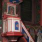 Zdjęcie nr 1: Ambona przyścienna, wisząca, z dostępem od wschodu w postaci jednobiegowych schodów z balustradą. Kosz na planie kwadratu o ściętych narożach, na podstawie w formie wałka, z podwieszeniem o wklęsłych bokach, zakończonym gzymsem. Zachodnia i południowa ścianka kosza ujęte pilastrami, parapet w formie profilowanego gzymsu. Ścianka frontowa ambony dekorowana płyciną w kształcie stojącego prostokąta o wciętych górnych narożach z rozetą w polu, zachodnia zaś liściem palmy. Balustrada schodów dekorowana dwoma płycinami z liśćmi palmowymi, poręcz w formie profilowanego gzymsu. Zaplecek w kształcie stojącego prostokąta ujętego spływami wolutowymi. W profilowanej płycinie o fantazyjnym wykroju malowane przedstawienie Matki Boskiej z Dzieciątkiem. Baldachim na planie kwadratu o ściętych narożach, zwieńczony wielobocznym postumentem, o wklęsłych ściankach, na którym znajduje się krzyż z czworoliściem w środku. Na skrzyżowaniu ramion krzyża wiązki promieni. Na podniebiu baldachimu, w ośmiobocznej płycinie gołębica Ducha Świętego w glorii promienistej. Struktura ambony polichromowana w kolorze białym, z czerwonymi cokołami, obramieniami i profilami, pola płycin niebieskie.  Pilastry kosza, pas balustrady, zaplecek i podniebie baldachimu dekorowane pozłoconym ornamentem geometrycznym.
