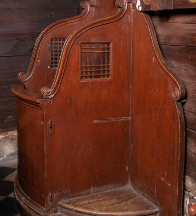 Zdjęcie nr 1: Konfesjonał na półkolistej podstawie. Pośrodku siedzisko z wysokim zapleckiem zakończonym dwoma impostami podtrzymującymi gzyms w formie łuku półkolistego nadwieszonego. Siedzisko ujęte dwoma wysokimi ściankami bocznymi o esowatym wykroju, w górnej połowie kwadratowe otwory z kratownicą. Drzwiczki w partii przedpiersia, sięgające połowy wysokości ścianek bocznych, lekko wypukłe, zakończone gzymsem. Po bokach siedziska dwustopniowe klęczniki. Boczne części zaplecka o fantazyjnym wykroju zakończone esowatymi spływami wolutowymi. Całość politurowana, w kolorze naturalnego drewna. 


