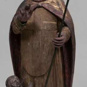 Zdjęcie nr 1: Figura nieopracowana rzeźbiarsko z tyłu, ustawiona jest na niewielkiej, nieregularnej podstawie. Święty ukazany jest w całej postaci, frontalnie, z głową skierowaną w prawo. Prawą rękę unosi delikatnie w geście błogosławieństwa, w lewej wyciągniętej do przodu trzyma laskę zakończoną krzyżem. Jego twarz jest trójkątna, o półprzymkniętych oczach, niewielkim nosie i wąskich ustach. Ubrany jest w albę, ornat z płaskorzeźbioną krzyżową pretekstą, kapę zapiętą na piersi, na głowie ma infułę. Przy jego prawej nodze znajduje się półpostać Piotrowina, zwróconego ku świętemu,  z rękoma złożonymi w geście modlitwy, nakrytego płaszczem. Polichromia w odsłoniętych partiach karnacji obecnie poszarzała, strój złocony. 







