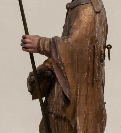 Zdjęcie nr 3: Figura nieopracowana z tyłu, ustawiona na niewielkiej podstawie. Święty ukazany jest w całej postaci, frontalnie, w kontrapoście, z pochyloną głową skierowaną w lewo. W prawej, opuszczonej wzdłuż ciała ręce trzyma zamkniętą księgę, w lewej, uniesionej przed sobą na wysokości piersi – wiosło. Jego twarz jest trójkątna o migdałowatych oczach, krótkim nosie i wąskich ustach, okolona brodą. Ubrany jest w albę, rokietę oraz płaszcz z kołnierzem zapięty pod szyją, na głowie ma infułę. Polichromia naturalistyczna w partiach ciała, strój i atrybuty złocone. 
