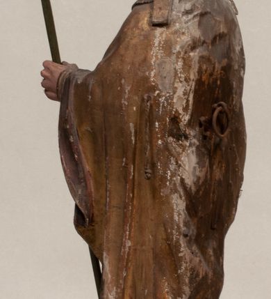 Zdjęcie nr 6: Figura nieopracowana z tyłu, ustawiona na niewielkiej podstawie. Święty ukazany jest w całej postaci, frontalnie, w kontrapoście, z pochyloną głową skierowaną w lewo. W prawej, opuszczonej wzdłuż ciała ręce trzyma zamkniętą księgę, w lewej, uniesionej przed sobą na wysokości piersi – wiosło. Jego twarz jest trójkątna o migdałowatych oczach, krótkim nosie i wąskich ustach, okolona brodą. Ubrany jest w albę, rokietę oraz płaszcz z kołnierzem zapięty pod szyją, na głowie ma infułę. Polichromia naturalistyczna w partiach ciała, strój i atrybuty złocone. 
