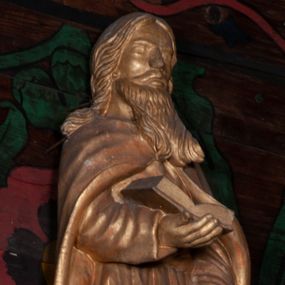 Zdjęcie nr 1: Rzeźba jest ścięta i drążona z tyłu, ustawiona na niskiej podstawie na planie półkola. Święty przedstawiony w całej postaci, zwrócony jest frontalnie, z ugiętą prawą nogą. W prawej, ugiętej ręce podtrzymuje na wysokości talii otwartą księgę, lewa jest wyprostowana, opuszczona w dół. Twarz ma kwadratową, o migdałowatych oczach, krótkim nosie i pełnych ustach, okoloną długą brodą opadającą na pierś oraz długimi, skręconymi włosami sięgającymi ramion. Święty ubrany jest w tunikę przepasaną w talii oraz płaszcz zapięty na piersi, opadający na ramiona i plecy postaci. Figura w całości polichromowana w kolorze złotym.
