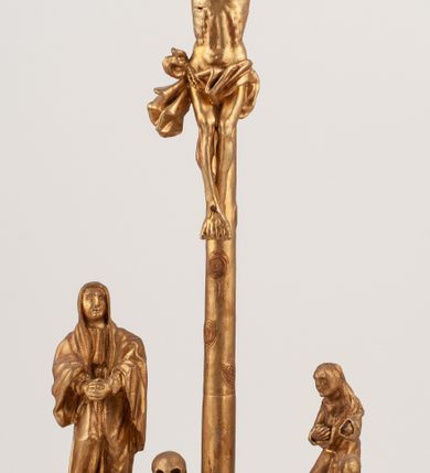 Zdjęcie nr 2: Grupa Ukrzyżowania umieszczona jest na wysokim cokole z ryzalitem pośrodku, profilowanym u dołu i zakończonym gzymsem z kostkowaniem. Do cokołu z trzech stron przytwierdzone są gwoździkami płaskorzeźbione narzędzia Męki Pańskiej. Grupa ustawiona jest na rzeźbionym podłożu imitującym skałę. Pośrodku znajduje się krzyż z pnia drzewa, do którego przybita jest trzema gwoździami figurka umarłego Chrystusa. Jego ciało jest w dużym zwisie, o ramionach przyjmujących kształt łuku półkolistego, głowa opada na prawy bark, nogi ułożone są równolegle, stopy skrzyżowane w układzie prawa na lewą. Twarz pociągła, okolona krótką brodą oraz silnie kręconymi włosami, na głowie korona cierniowa. Ciało smukłe, z podkreślonymi żebrami klatki piersiowej i zaznaczonymi śladami męki. Biodra przepasane krótkim, ekspresyjnie drapowanym perizonium, zawieszonym na podwójnym sznurze, odsłaniającym prawe biodro, zawiązanym na prawym boku. Pionowa belka krzyża zakończona banderolą z rytym napisem „IN / RI”. U podstawy krzyża znajduje się czaszka z piszczelami. 
Po prawej stronie krzyża stoi Maria ze splecionymi z przodu dłońmi. Ubrana jest w tunikę, przepasaną w talii oraz płaszcz narzucony na głowę i ramiona. Po lewej stronie znajduje się św. Jan. Zwrócony jest w trzech czwartych w prawo, klęczy na prawym kolanie i prawą dłoń kładzie na piersi, lewą rękę wyciąga do przodu. Jego twarz okalają długie włosy opadające na ramiona. Ubrany jest w tunikę, przepasaną w talii. 
Figury oraz detale rzeźbiarskie i profile cokołu pozłocone, struktura cokołu polichromowana na czarno. 