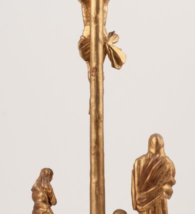 Zdjęcie nr 3: Grupa Ukrzyżowania umieszczona jest na wysokim cokole z ryzalitem pośrodku, profilowanym u dołu i zakończonym gzymsem z kostkowaniem. Do cokołu z trzech stron przytwierdzone są gwoździkami płaskorzeźbione narzędzia Męki Pańskiej. Grupa ustawiona jest na rzeźbionym podłożu imitującym skałę. Pośrodku znajduje się krzyż z pnia drzewa, do którego przybita jest trzema gwoździami figurka umarłego Chrystusa. Jego ciało jest w dużym zwisie, o ramionach przyjmujących kształt łuku półkolistego, głowa opada na prawy bark, nogi ułożone są równolegle, stopy skrzyżowane w układzie prawa na lewą. Twarz pociągła, okolona krótką brodą oraz silnie kręconymi włosami, na głowie korona cierniowa. Ciało smukłe, z podkreślonymi żebrami klatki piersiowej i zaznaczonymi śladami męki. Biodra przepasane krótkim, ekspresyjnie drapowanym perizonium, zawieszonym na podwójnym sznurze, odsłaniającym prawe biodro, zawiązanym na prawym boku. Pionowa belka krzyża zakończona banderolą z rytym napisem „IN / RI”. U podstawy krzyża znajduje się czaszka z piszczelami. 
Po prawej stronie krzyża stoi Maria ze splecionymi z przodu dłońmi. Ubrana jest w tunikę, przepasaną w talii oraz płaszcz narzucony na głowę i ramiona. Po lewej stronie znajduje się św. Jan. Zwrócony jest w trzech czwartych w prawo, klęczy na prawym kolanie i prawą dłoń kładzie na piersi, lewą rękę wyciąga do przodu. Jego twarz okalają długie włosy opadające na ramiona. Ubrany jest w tunikę, przepasaną w talii. 
Figury oraz detale rzeźbiarskie i profile cokołu pozłocone, struktura cokołu polichromowana na czarno. 