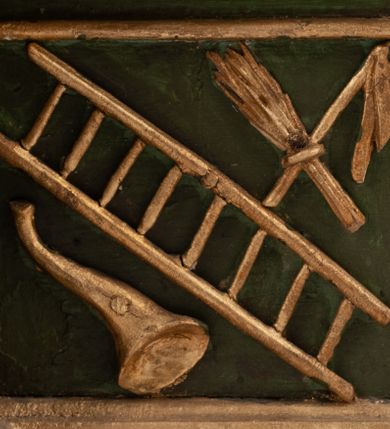 Zdjęcie nr 16: Grupa Ukrzyżowania umieszczona jest na wysokim cokole z ryzalitem pośrodku, profilowanym u dołu i zakończonym gzymsem z kostkowaniem. Do cokołu z trzech stron przytwierdzone są gwoździkami płaskorzeźbione narzędzia Męki Pańskiej. Grupa ustawiona jest na rzeźbionym podłożu imitującym skałę. Pośrodku znajduje się krzyż z pnia drzewa, do którego przybita jest trzema gwoździami figurka umarłego Chrystusa. Jego ciało jest w dużym zwisie, o ramionach przyjmujących kształt łuku półkolistego, głowa opada na prawy bark, nogi ułożone są równolegle, stopy skrzyżowane w układzie prawa na lewą. Twarz pociągła, okolona krótką brodą oraz silnie kręconymi włosami, na głowie korona cierniowa. Ciało smukłe, z podkreślonymi żebrami klatki piersiowej i zaznaczonymi śladami męki. Biodra przepasane krótkim, ekspresyjnie drapowanym perizonium, zawieszonym na podwójnym sznurze, odsłaniającym prawe biodro, zawiązanym na prawym boku. Pionowa belka krzyża zakończona banderolą z rytym napisem „IN / RI”. U podstawy krzyża znajduje się czaszka z piszczelami. 
Po prawej stronie krzyża stoi Maria ze splecionymi z przodu dłońmi. Ubrana jest w tunikę, przepasaną w talii oraz płaszcz narzucony na głowę i ramiona. Po lewej stronie znajduje się św. Jan. Zwrócony jest w trzech czwartych w prawo, klęczy na prawym kolanie i prawą dłoń kładzie na piersi, lewą rękę wyciąga do przodu. Jego twarz okalają długie włosy opadające na ramiona. Ubrany jest w tunikę, przepasaną w talii. 
Figury oraz detale rzeźbiarskie i profile cokołu pozłocone, struktura cokołu polichromowana na czarno. 