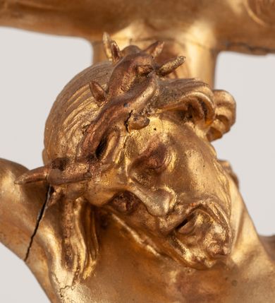 Zdjęcie nr 6: Grupa Ukrzyżowania umieszczona jest na wysokim cokole z ryzalitem pośrodku, profilowanym u dołu i zakończonym gzymsem z kostkowaniem. Do cokołu z trzech stron przytwierdzone są gwoździkami płaskorzeźbione narzędzia Męki Pańskiej. Grupa ustawiona jest na rzeźbionym podłożu imitującym skałę. Pośrodku znajduje się krzyż z pnia drzewa, do którego przybita jest trzema gwoździami figurka umarłego Chrystusa. Jego ciało jest w dużym zwisie, o ramionach przyjmujących kształt łuku półkolistego, głowa opada na prawy bark, nogi ułożone są równolegle, stopy skrzyżowane w układzie prawa na lewą. Twarz pociągła, okolona krótką brodą oraz silnie kręconymi włosami, na głowie korona cierniowa. Ciało smukłe, z podkreślonymi żebrami klatki piersiowej i zaznaczonymi śladami męki. Biodra przepasane krótkim, ekspresyjnie drapowanym perizonium, zawieszonym na podwójnym sznurze, odsłaniającym prawe biodro, zawiązanym na prawym boku. Pionowa belka krzyża zakończona banderolą z rytym napisem „IN / RI”. U podstawy krzyża znajduje się czaszka z piszczelami. 
Po prawej stronie krzyża stoi Maria ze splecionymi z przodu dłońmi. Ubrana jest w tunikę, przepasaną w talii oraz płaszcz narzucony na głowę i ramiona. Po lewej stronie znajduje się św. Jan. Zwrócony jest w trzech czwartych w prawo, klęczy na prawym kolanie i prawą dłoń kładzie na piersi, lewą rękę wyciąga do przodu. Jego twarz okalają długie włosy opadające na ramiona. Ubrany jest w tunikę, przepasaną w talii. 
Figury oraz detale rzeźbiarskie i profile cokołu pozłocone, struktura cokołu polichromowana na czarno. 