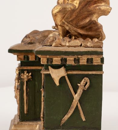 Zdjęcie nr 14: Grupa Ukrzyżowania umieszczona jest na wysokim cokole z ryzalitem pośrodku, profilowanym u dołu i zakończonym gzymsem z kostkowaniem. Do cokołu z trzech stron przytwierdzone są gwoździkami płaskorzeźbione narzędzia Męki Pańskiej. Grupa ustawiona jest na rzeźbionym podłożu imitującym skałę. Pośrodku znajduje się krzyż z pnia drzewa, do którego przybita jest trzema gwoździami figurka umarłego Chrystusa. Jego ciało jest w dużym zwisie, o ramionach przyjmujących kształt łuku półkolistego, głowa opada na prawy bark, nogi ułożone są równolegle, stopy skrzyżowane w układzie prawa na lewą. Twarz pociągła, okolona krótką brodą oraz silnie kręconymi włosami, na głowie korona cierniowa. Ciało smukłe, z podkreślonymi żebrami klatki piersiowej i zaznaczonymi śladami męki. Biodra przepasane krótkim, ekspresyjnie drapowanym perizonium, zawieszonym na podwójnym sznurze, odsłaniającym prawe biodro, zawiązanym na prawym boku. Pionowa belka krzyża zakończona banderolą z rytym napisem „IN / RI”. U podstawy krzyża znajduje się czaszka z piszczelami. 
Po prawej stronie krzyża stoi Maria ze splecionymi z przodu dłońmi. Ubrana jest w tunikę, przepasaną w talii oraz płaszcz narzucony na głowę i ramiona. Po lewej stronie znajduje się św. Jan. Zwrócony jest w trzech czwartych w prawo, klęczy na prawym kolanie i prawą dłoń kładzie na piersi, lewą rękę wyciąga do przodu. Jego twarz okalają długie włosy opadające na ramiona. Ubrany jest w tunikę, przepasaną w talii. 
Figury oraz detale rzeźbiarskie i profile cokołu pozłocone, struktura cokołu polichromowana na czarno. 