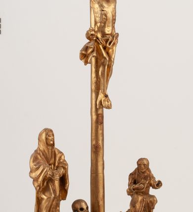 Zdjęcie nr 7: Grupa Ukrzyżowania umieszczona jest na wysokim cokole z ryzalitem pośrodku, profilowanym u dołu i zakończonym gzymsem z kostkowaniem. Do cokołu z trzech stron przytwierdzone są gwoździkami płaskorzeźbione narzędzia Męki Pańskiej. Grupa ustawiona jest na rzeźbionym podłożu imitującym skałę. Pośrodku znajduje się krzyż z pnia drzewa, do którego przybita jest trzema gwoździami figurka umarłego Chrystusa. Jego ciało jest w dużym zwisie, o ramionach przyjmujących kształt łuku półkolistego, głowa opada na prawy bark, nogi ułożone są równolegle, stopy skrzyżowane w układzie prawa na lewą. Twarz pociągła, okolona krótką brodą oraz silnie kręconymi włosami, na głowie korona cierniowa. Ciało smukłe, z podkreślonymi żebrami klatki piersiowej i zaznaczonymi śladami męki. Biodra przepasane krótkim, ekspresyjnie drapowanym perizonium, zawieszonym na podwójnym sznurze, odsłaniającym prawe biodro, zawiązanym na prawym boku. Pionowa belka krzyża zakończona banderolą z rytym napisem „IN / RI”. U podstawy krzyża znajduje się czaszka z piszczelami. 
Po prawej stronie krzyża stoi Maria ze splecionymi z przodu dłońmi. Ubrana jest w tunikę, przepasaną w talii oraz płaszcz narzucony na głowę i ramiona. Po lewej stronie znajduje się św. Jan. Zwrócony jest w trzech czwartych w prawo, klęczy na prawym kolanie i prawą dłoń kładzie na piersi, lewą rękę wyciąga do przodu. Jego twarz okalają długie włosy opadające na ramiona. Ubrany jest w tunikę, przepasaną w talii. 
Figury oraz detale rzeźbiarskie i profile cokołu pozłocone, struktura cokołu polichromowana na czarno. 