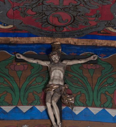 Zdjęcie nr 2: Figura umarłego Chrystusa przybita jest do krzyża o prostych ramionach czterema gwoździami. Ciało w lekkim zwisie o horyzontalnie rozłożonych ramionach, głowa bezwładnie opada na prawe ramię, nogi ugięte w kolanach, skierowane w prawo. Twarz Chrystusa jest pociągła, o zamkniętych oczach, prostym, długim nosie oraz pełnych, rozchylonych ustach, okolona krótką brodą oraz delikatnie kręconymi włosami opadającymi na prawe ramię. Na głowie ma koronę cierniową. Ciało wychudzone, o silnie zaznaczonej muskulaturze rąk i nóg, wyraźnie podkreślonych żebrach klatki piersiowej i zapadłym brzuchu. Biodra przepasane są krótkim perizonium zawieszonym na sznurze, z rozwianym zwisem tkaniny przy lewym boku. Polichromia ciała naturalistyczna z zaznaczonymi śladami męki, korona cierniowa i perizonium pozłocone. 

