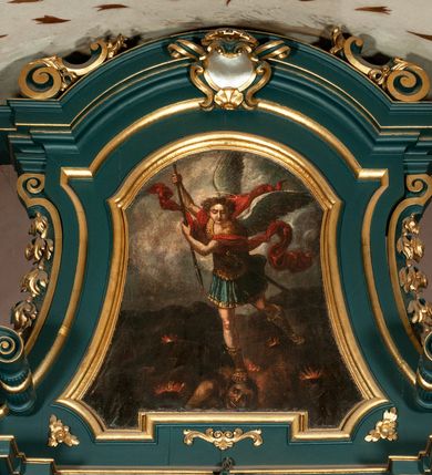 Zdjęcie nr 2: Obraz o nieregularnym, wklęsło-wypukłym kształcie dopasowanym do zwieńczenia ołtarza. W centrum kompozycji znajduje się święty Michał Archanioł w dynamicznej pozie, strącający szatana do piekła. Archanioł ukazany w postawie stojącej, z lewą nogą cofniętą do tyłu, prawą depczący głowę szatana, z podniesionymi do góry rękami, w których trzyma włócznię skierowaną ostrzem w dół. Twarz archanioła szeroka, z długim i prostym nosem, wzrokiem skierowanym w dół. Włosy średniej długości, kręcone, rozwiane do tyłu. Ubrany w zbroję legionisty rzymskiego (złoty pancerz, niebieska tunika, wysokiem złote sandały) z czerwonym płaszczem rozwianym na wietrze, u pleców białe skrzydła, nad głową złoty i okrągły nimb. Dół kompozycji zajmuje skaliste, ciemne podłoże, z którego wydobywają się płomienie. Szatan ukazany w monstrualnej postaci, ze skrzydłami nietoperza, w postawie leżącej. W górnej części obrazu tło pochmurne, ciemne. Rama drewniana, złocona, polichromowana. 

