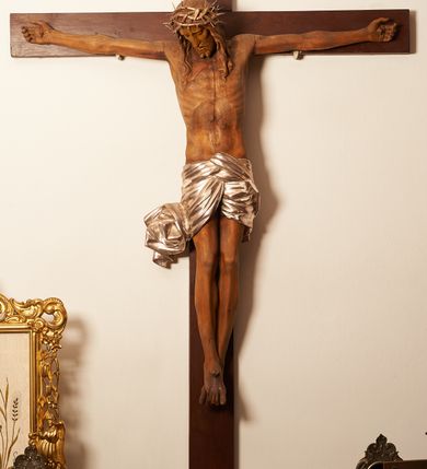 Zdjęcie nr 2: Rzeźbiona figura Chrystusa Ukrzyżowanego zawieszona na prostym, późniejszym od rzeźby krzyżu. Chrustu wisi z rozłożonymi do boków rękami przybitymi gwoździami, ze stopami złożonymi razem, prawa na lewej, przybitymi jednym gwoździem; kolana lekko ugięte. Ciało wyprężone, z zaznaczonymi żebrami i muskulaturą. Głowa opada na prawe ramię, twarz pociągła, oczy przymknięte, proste, nos prosty, długi, usta rozchylone, otoczone krótkimi wąsami i dzieląca się w dwa pukle brodą. Długie, kręcone włosy opadają do przodu, na tors, na głowie masywna, złocona korona cierniowa. Figura bejcowana na kolor ciemnobrązowy. Biodra przewiązane srebrzonym, krótkim perizonium którego zwoje przeplatają się z przodu, a koniec przy prawym udzie zawija się w ekspresyjny zwój. Tkanina układa się w drobne fałdy. Chrystus wisi na drewnianym, ciemnobrązowym krzyżu, w jej górnej części titulus z napisem „I.N./R.I.”.  