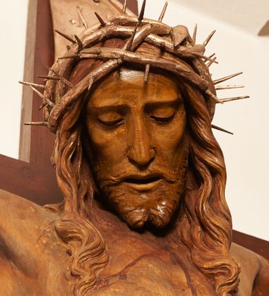 Zdjęcie nr 8: Rzeźbiona figura Chrystusa Ukrzyżowanego zawieszona na prostym, późniejszym od rzeźby krzyżu. Chrustu wisi z rozłożonymi do boków rękami przybitymi gwoździami, ze stopami złożonymi razem, prawa na lewej, przybitymi jednym gwoździem; kolana lekko ugięte. Ciało wyprężone, z zaznaczonymi żebrami i muskulaturą. Głowa opada na prawe ramię, twarz pociągła, oczy przymknięte, proste, nos prosty, długi, usta rozchylone, otoczone krótkimi wąsami i dzieląca się w dwa pukle brodą. Długie, kręcone włosy opadają do przodu, na tors, na głowie masywna, złocona korona cierniowa. Figura bejcowana na kolor ciemnobrązowy. Biodra przewiązane srebrzonym, krótkim perizonium którego zwoje przeplatają się z przodu, a koniec przy prawym udzie zawija się w ekspresyjny zwój. Tkanina układa się w drobne fałdy. Chrystus wisi na drewnianym, ciemnobrązowym krzyżu, w jej górnej części titulus z napisem „I.N./R.I.”.  