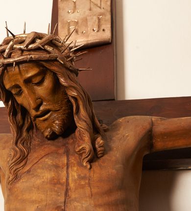 Zdjęcie nr 14: Rzeźbiona figura Chrystusa Ukrzyżowanego zawieszona na prostym, późniejszym od rzeźby krzyżu. Chrustu wisi z rozłożonymi do boków rękami przybitymi gwoździami, ze stopami złożonymi razem, prawa na lewej, przybitymi jednym gwoździem; kolana lekko ugięte. Ciało wyprężone, z zaznaczonymi żebrami i muskulaturą. Głowa opada na prawe ramię, twarz pociągła, oczy przymknięte, proste, nos prosty, długi, usta rozchylone, otoczone krótkimi wąsami i dzieląca się w dwa pukle brodą. Długie, kręcone włosy opadają do przodu, na tors, na głowie masywna, złocona korona cierniowa. Figura bejcowana na kolor ciemnobrązowy. Biodra przewiązane srebrzonym, krótkim perizonium którego zwoje przeplatają się z przodu, a koniec przy prawym udzie zawija się w ekspresyjny zwój. Tkanina układa się w drobne fałdy. Chrystus wisi na drewnianym, ciemnobrązowym krzyżu, w jej górnej części titulus z napisem „I.N./R.I.”.  