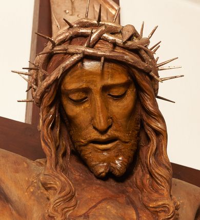 Zdjęcie nr 9: Rzeźbiona figura Chrystusa Ukrzyżowanego zawieszona na prostym, późniejszym od rzeźby krzyżu. Chrustu wisi z rozłożonymi do boków rękami przybitymi gwoździami, ze stopami złożonymi razem, prawa na lewej, przybitymi jednym gwoździem; kolana lekko ugięte. Ciało wyprężone, z zaznaczonymi żebrami i muskulaturą. Głowa opada na prawe ramię, twarz pociągła, oczy przymknięte, proste, nos prosty, długi, usta rozchylone, otoczone krótkimi wąsami i dzieląca się w dwa pukle brodą. Długie, kręcone włosy opadają do przodu, na tors, na głowie masywna, złocona korona cierniowa. Figura bejcowana na kolor ciemnobrązowy. Biodra przewiązane srebrzonym, krótkim perizonium którego zwoje przeplatają się z przodu, a koniec przy prawym udzie zawija się w ekspresyjny zwój. Tkanina układa się w drobne fałdy. Chrystus wisi na drewnianym, ciemnobrązowym krzyżu, w jej górnej części titulus z napisem „I.N./R.I.”.  